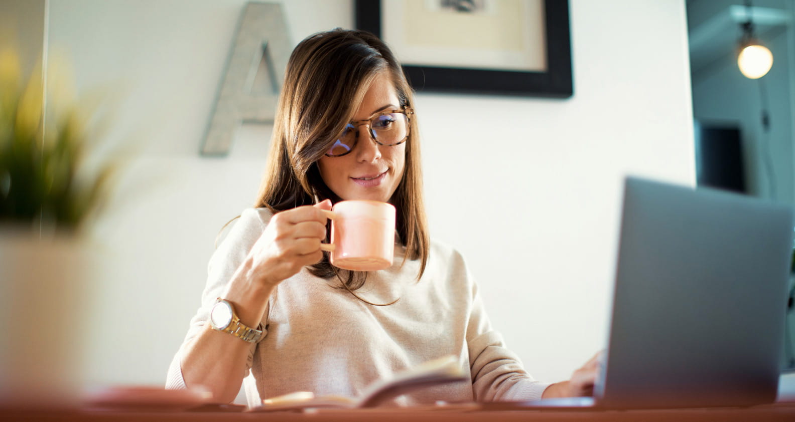 Young woman with cup of coffee working from home with laptop at desk